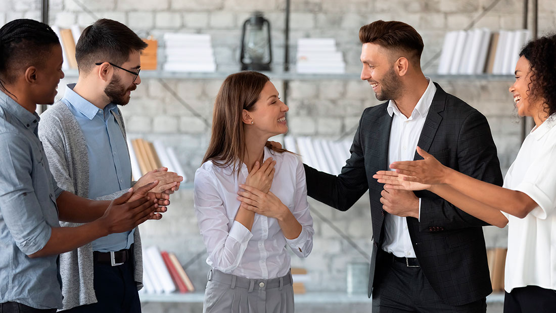 Cinco personas empresarias sonriendo y animando a compañera de trabajo