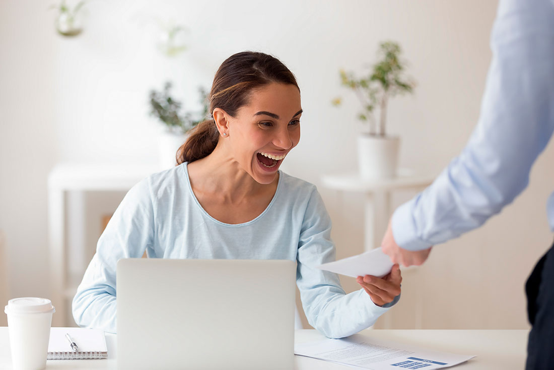 Mujer sentada frente a una laptop sonriendo mientras recibe un sobre 