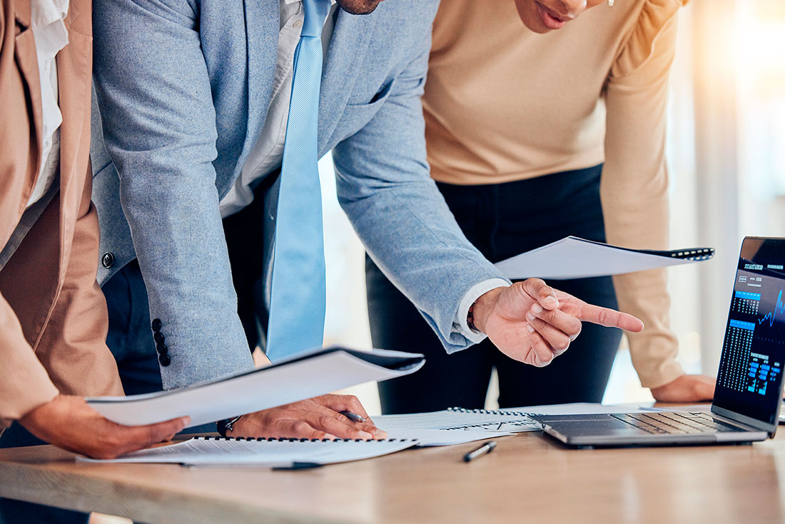 Toma de decisiones programadas Tres personas empresarias sosteniendo hojas frente a laptop con gráficas