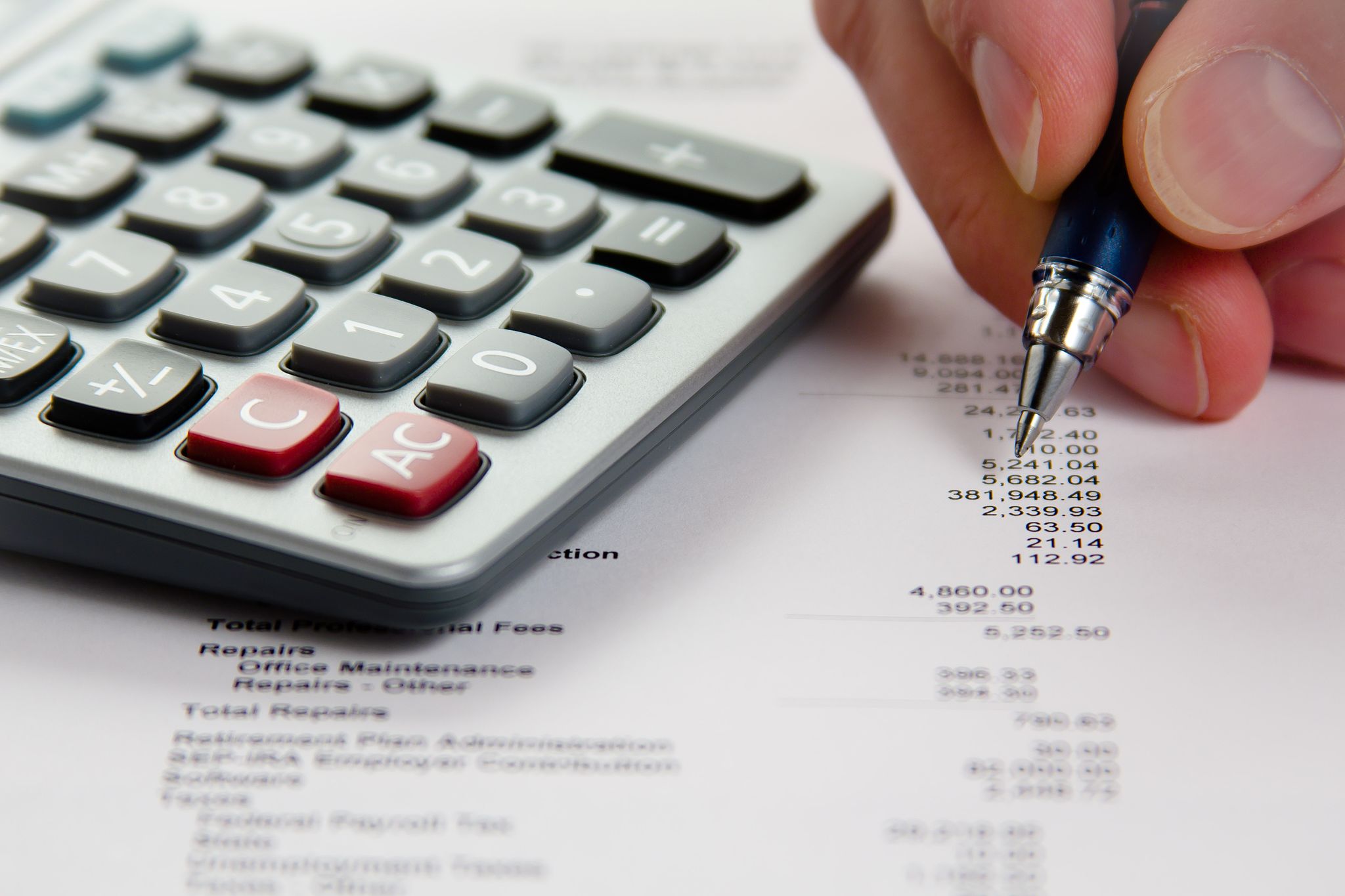 Primer plano de calculadora, mano, pluma y estado financiero.