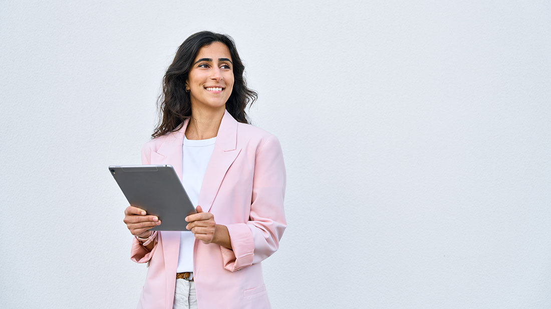 Mujer empresaria vistiendo saco rosa sosteniendo una tablet y sonriendo
