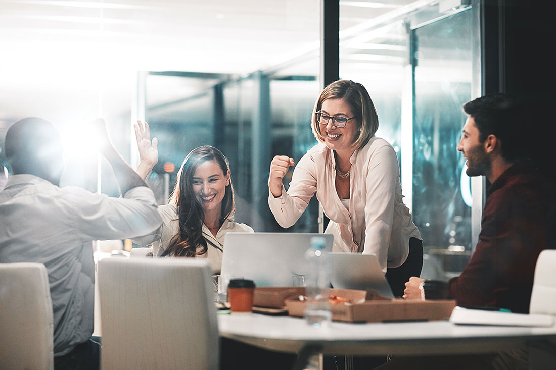 Cuatro personas reunidas alrededor de una mesa con diversos objetos sonriendo y estrechando la mano