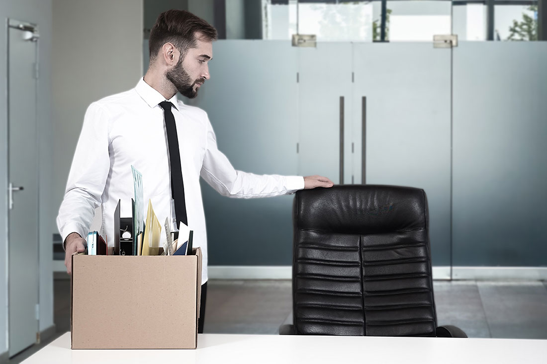 Hombre junto a una silla de oficina sosteniendo una caja con archivos y objetos diversos