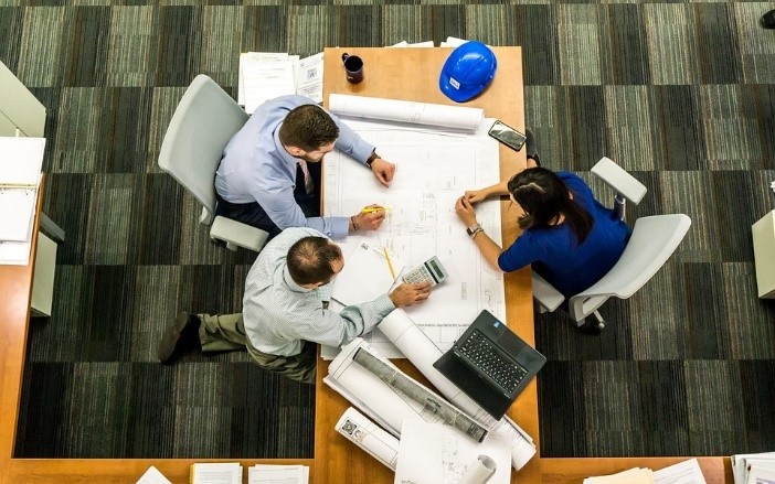 Grupo de tres personas sentadas alrededor de un escritorio con planos.