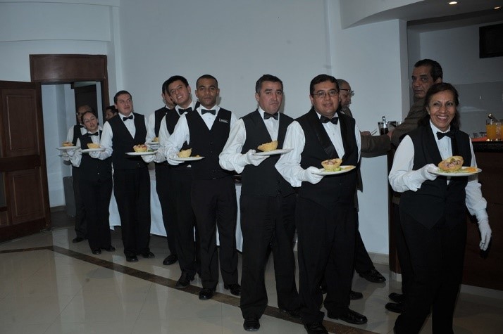 Grupo de meseros llevando platos sobre sus manos.