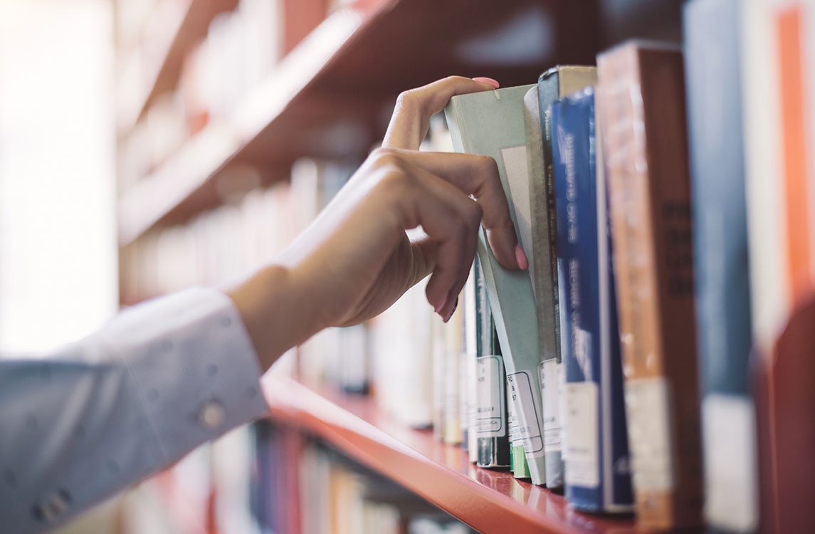 Mano de una persona tomando un libro de un estante en una biblioteca.