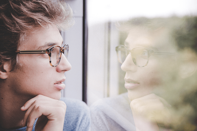 Fotografía de hombre de perfil frente a su imagen reflejada en una ventana