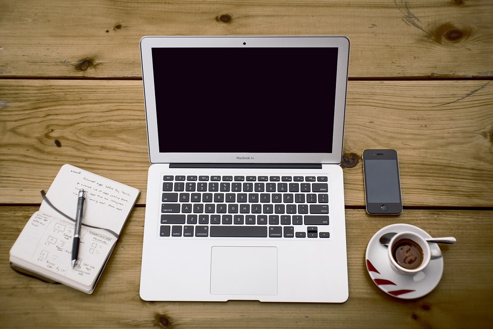 Imagen una computadora, bloc de notas, café y escritorio.
