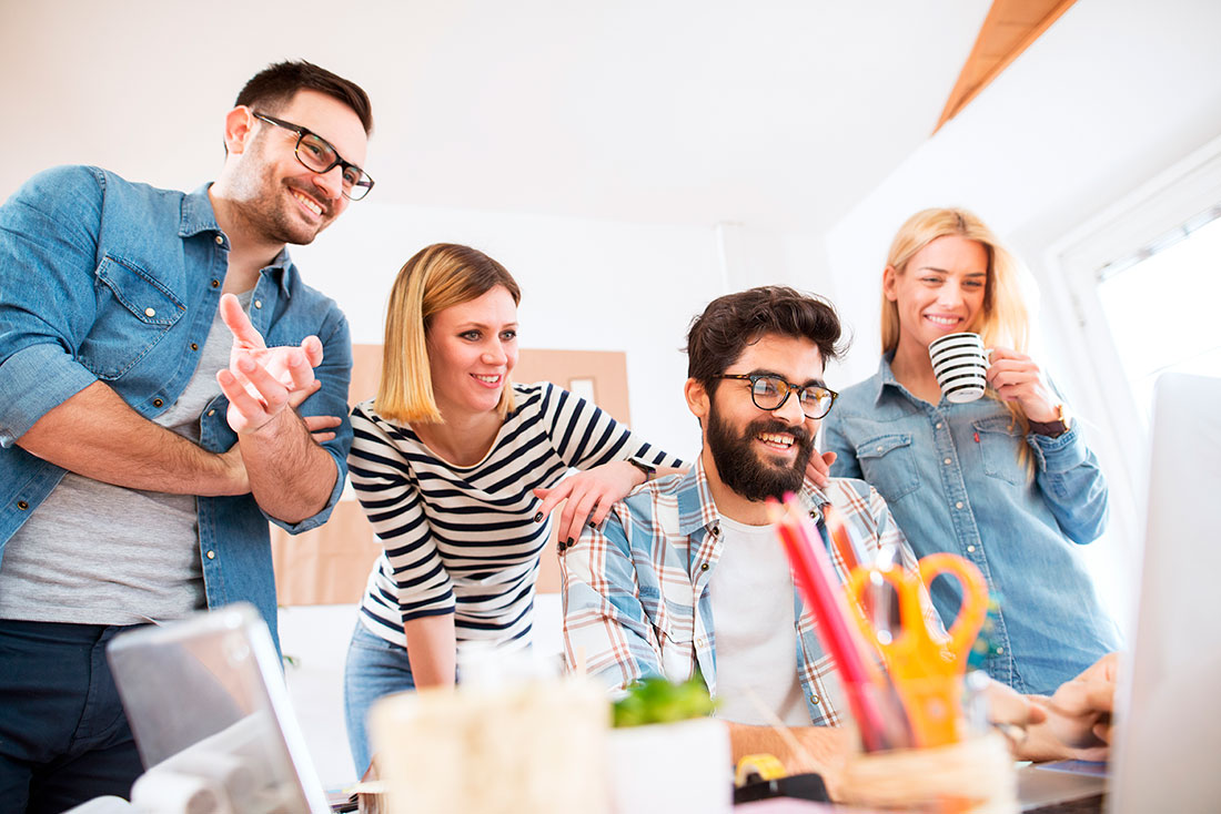 Cuatro compañeros de trabajo sonriendo frente a una laptop en una mesa con diferentes objetos