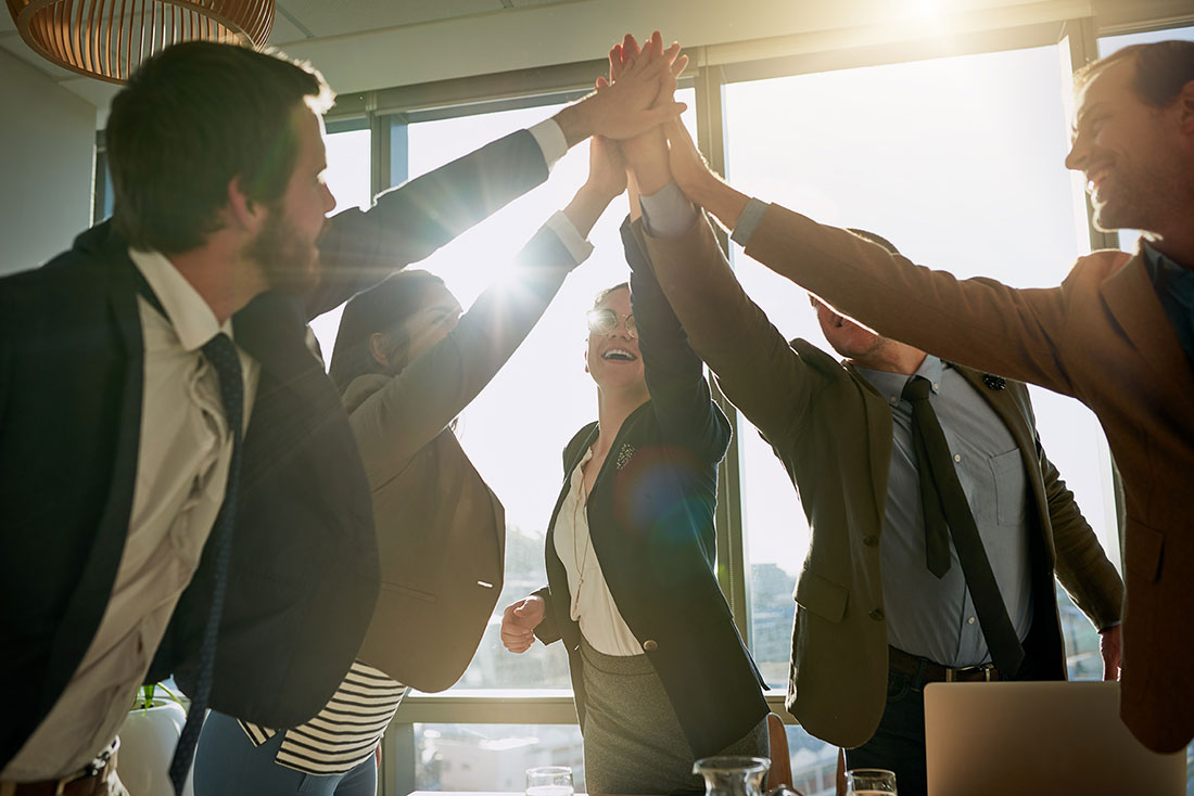 Cinco personas empresarias estrechando las manos y festejando en una oficina