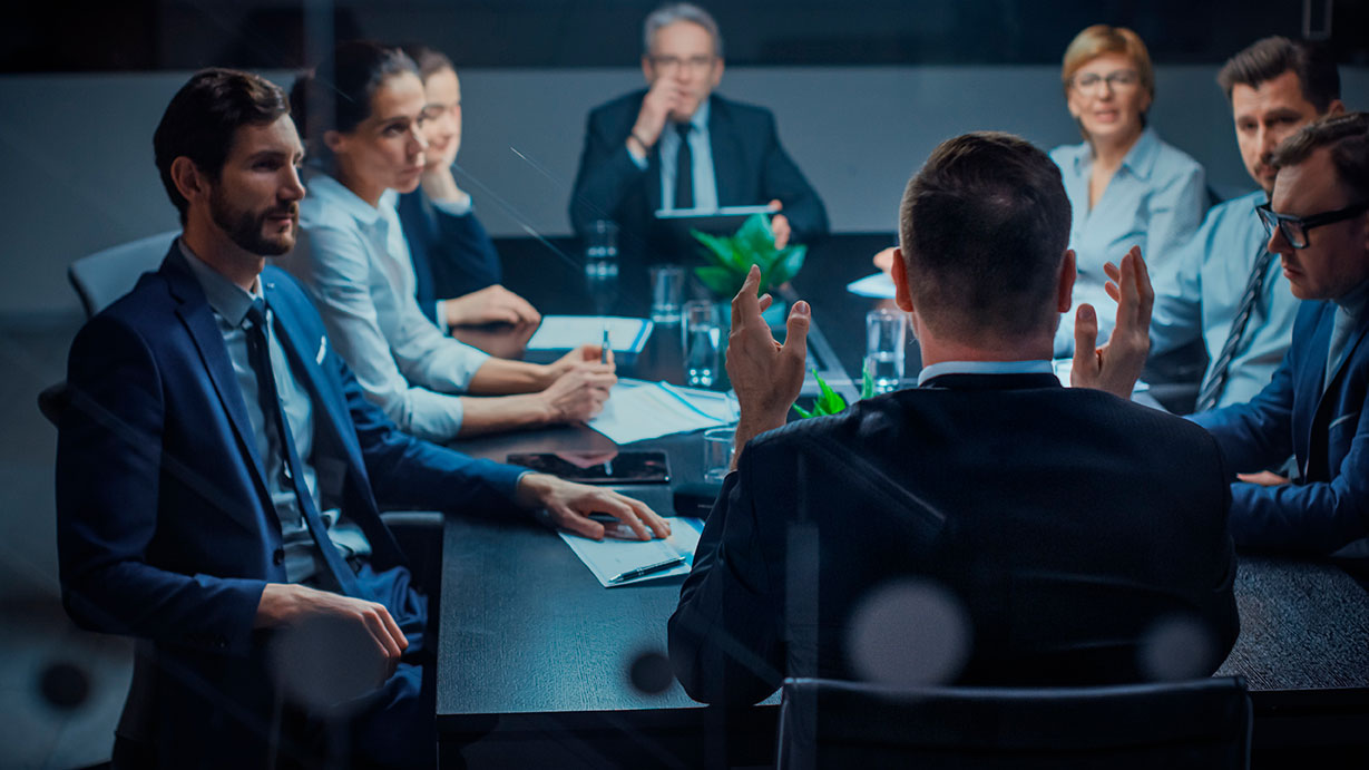 Personas con vestimenta formal sentadas alrededor de una mesa en una junta ejecutiva