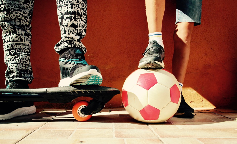 Pies de dos niños, el pie de uno sobre un balo y el del otro sobre una patineta
