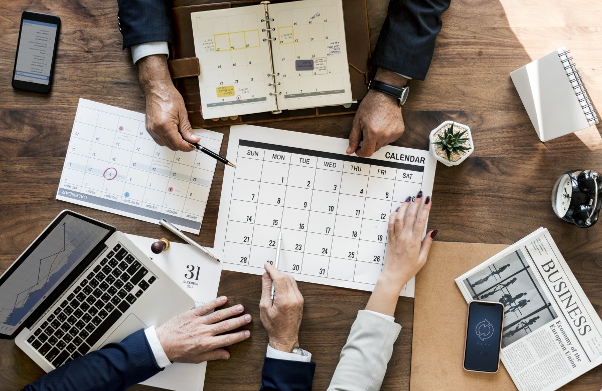 Imagen de un calendario en torno al cual trabajan tres personas, de quienes sólo se observan los antebrazos.