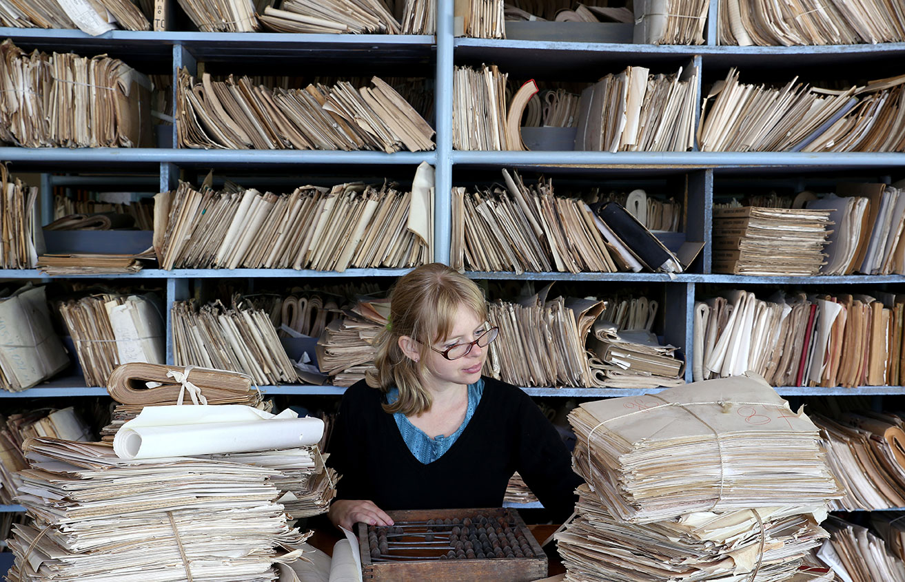 Mujer clasificando y archivando documentos antiguos en una estantería Mujer clasificando y archivando documentos antiguos en una estantería