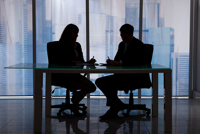 Dos personas empresarias sentadas frente a frente trabajando 