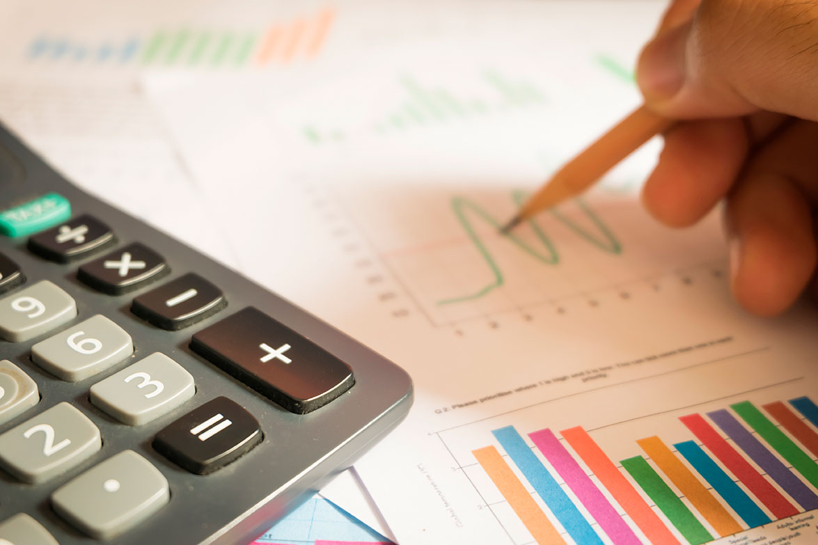 Persona sosteniendo un lápiz sobre hojas con gráficas y una calculadora