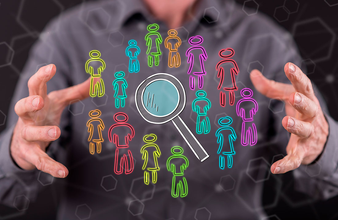 Iconos de personas de distintos colores y una lupa entre manos de un hombre