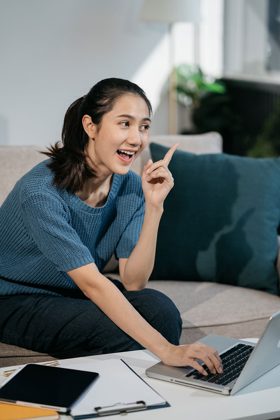 Mujer sentada frente a una laptop y una mesa con diferentes objetos pensando y sonriendo