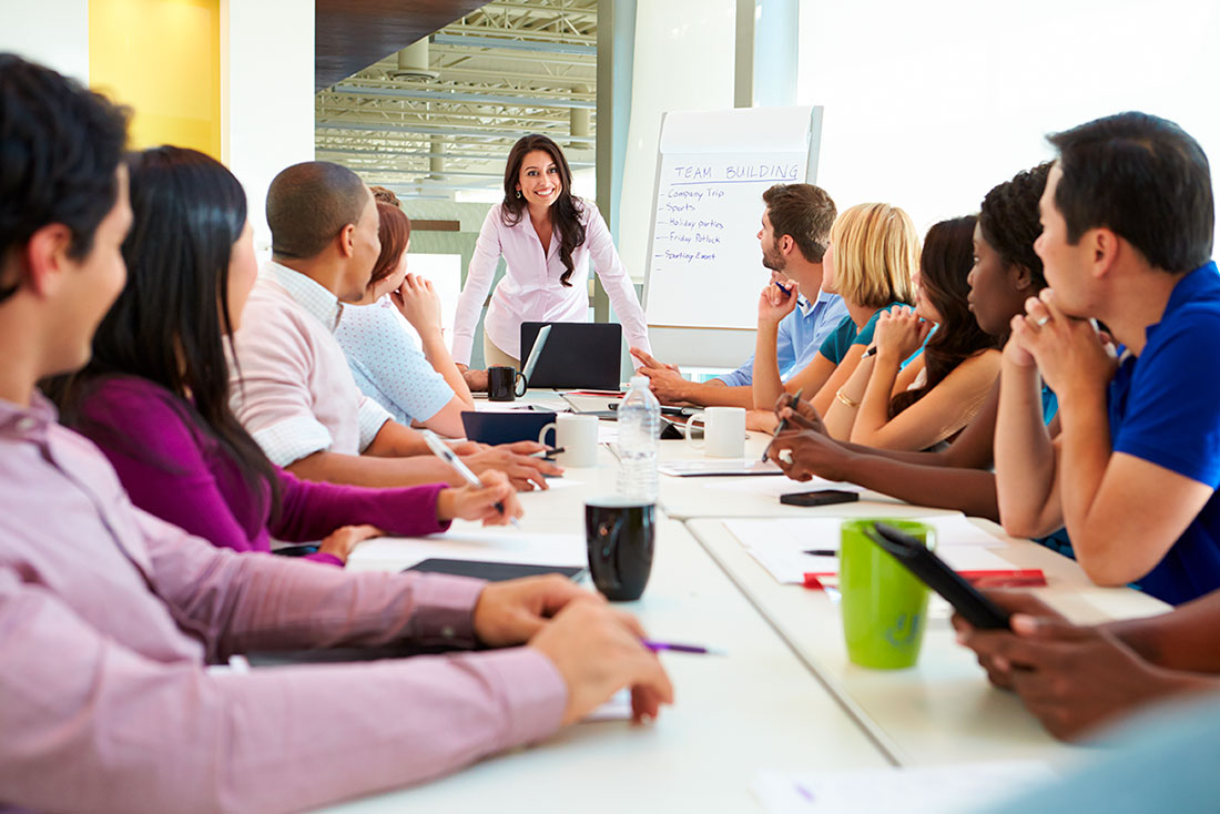 Grupo diverso de personas sentadas alrededor de una mesa en junta de trabajo