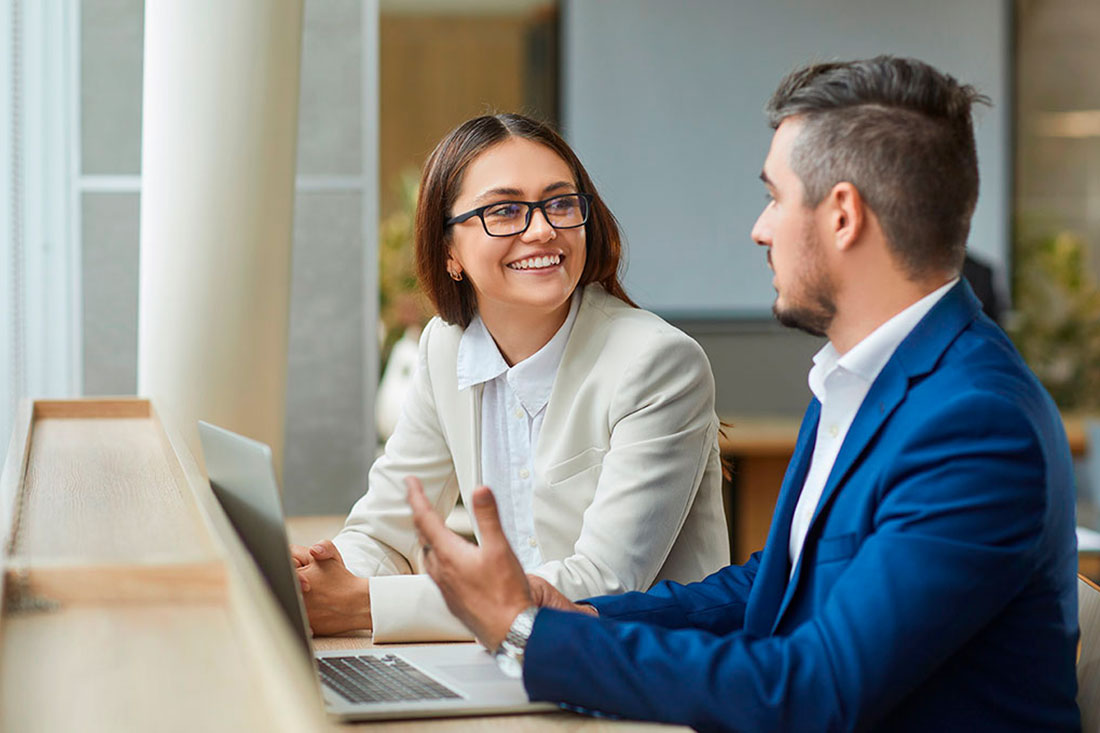 Dos personas empresarias sentadas frente a una laptop teniendo una conversación
