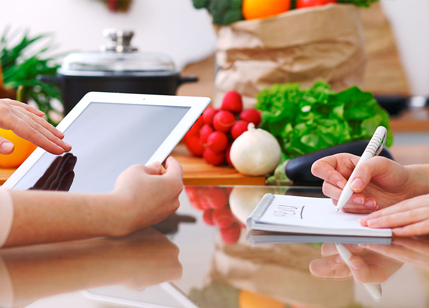 Acercamiento de las manos de cocineros usando una tableta, discutiendo el menú.