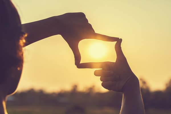Mujer con manos encuadrando el sol Manos de mujer haciendo un cuadro alrededor del sol