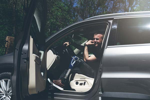 Hombre con prótesis en auto Hombre en auto con puerta abierta, usando prótesis en su pierna
