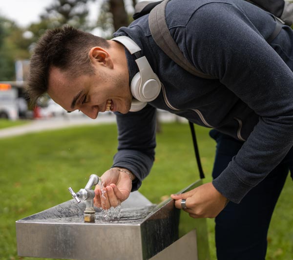 Hombre joven bebiendo agua de un bebedero