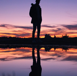 Una persona reflexionando y su reflejo en el agua.