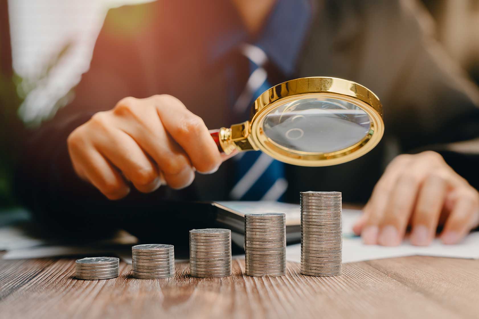 Hombre ejemplificando una auditoría financiera sosteniendo una lupa y analizando monedas 