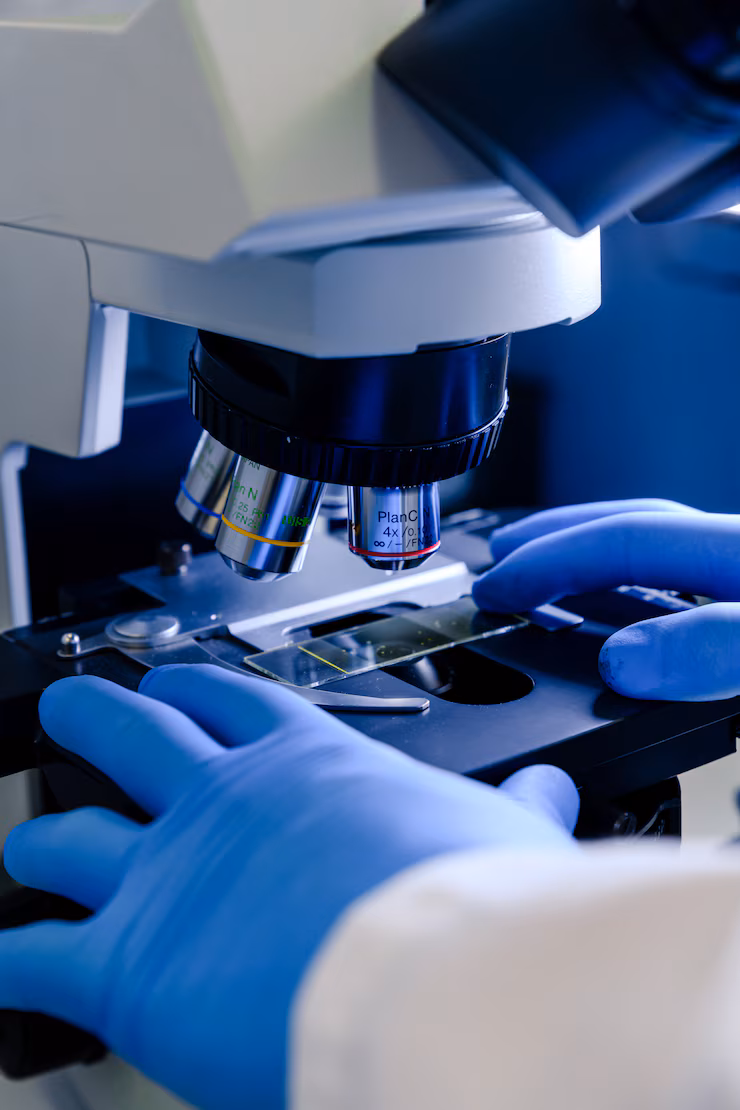 Manos con guantes clínicos y microscopio de laboratorio 